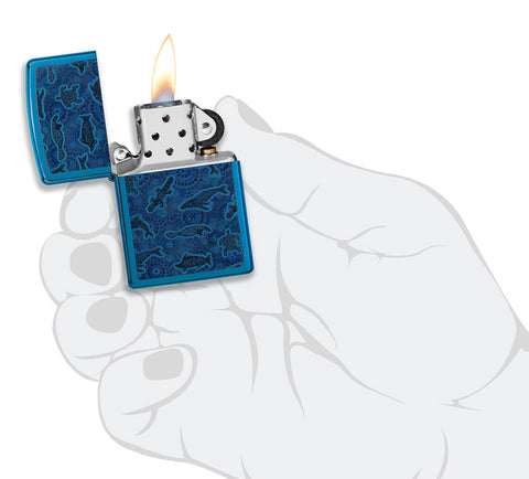 Zapalniczka Zippo z przodu otwarta i zapalona w kolorze niebieskim na wysoki połysk z ilustracją stworzenia morskiego w stylu sztuki aborygeńskiej w stylowej dłoni